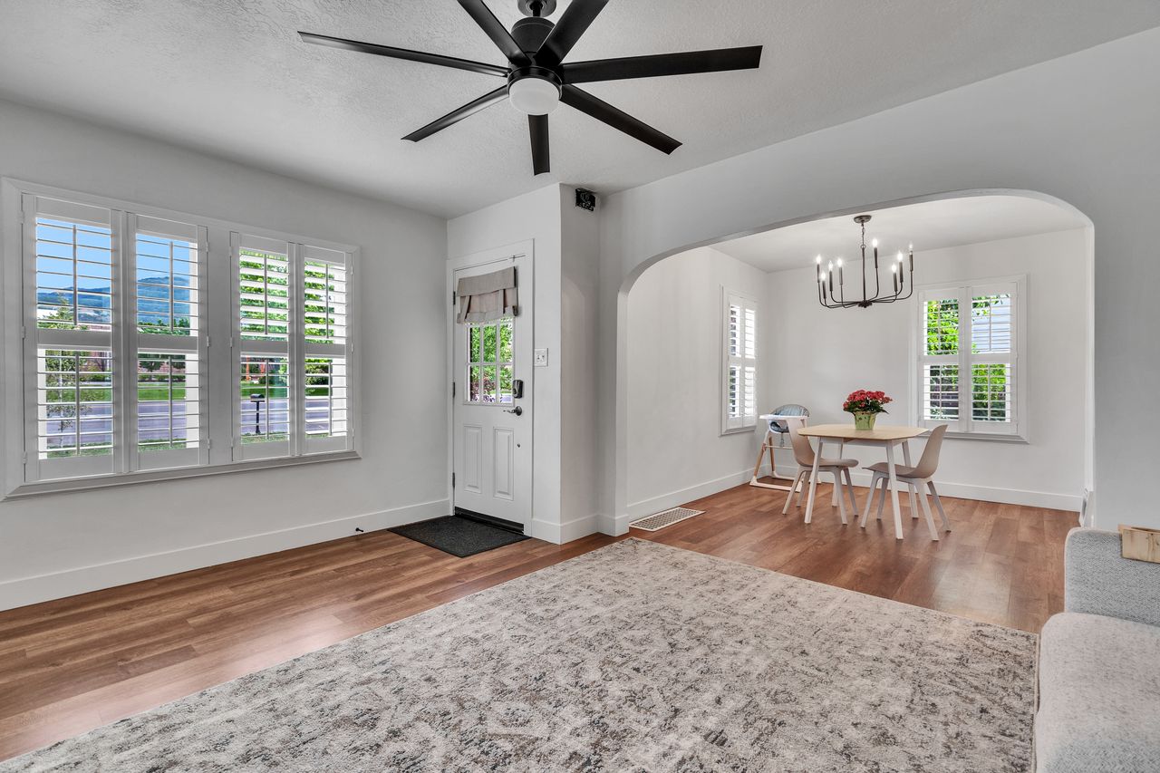 Living area featuring wood-finish flooring, a white paneled entry door, and a multi-pane window with plantation shutters