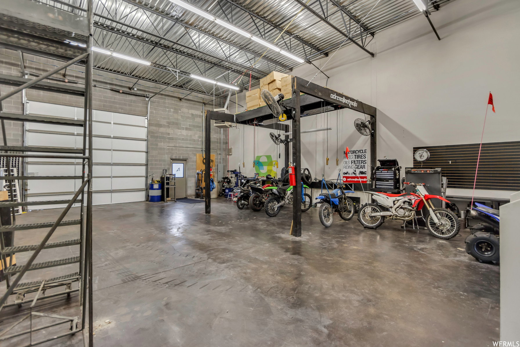 Spacious industrial-style garage featuring a large overhead door, concrete block walls, exposed metal truss ceiling, and concrete flooring