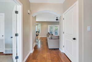 Hallway featuring wood-finish flooring, an arched entryway, white trim, and a paneled door with black hardware