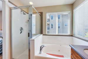 Full bathroom featuring a walk-in shower with a glass enclosure, a jetted soaking tub, and a vanity with a dark countertop