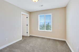 Neutral toned room featuring a window with horizontal blinds, gray carpet, white baseboards, and a white interior door