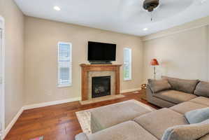 Living area featuring a fireplace with a wood-finish mantel and tile surround, wood-finish flooring, recessed lighting, and a ceiling fan