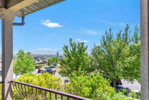 Balcony featuring a wrought iron railing and stucco column with recessed lighting, overlooking a neighborhood street, mature trees, and distant snow-capped mountains