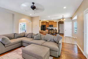 Open concept living area featuring wood-finish flooring, recessed lighting, an arched doorway, a ceiling fan, and access to the kitchen area with wood cabinetry