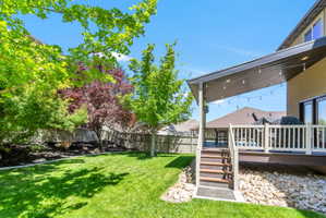 Expansive backyard featuring a covered deck with integrated lighting, wood-finish steps, and a white spindle railing