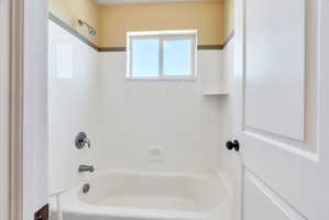 White bathtub and shower combination with a window, built-in soap dish, and chrome fixtures
