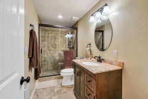 Bathroom with a glass-enclosed shower featuring decorative tile work, a vanity with a stone countertop, an undermount sink, and a framed oval mirror