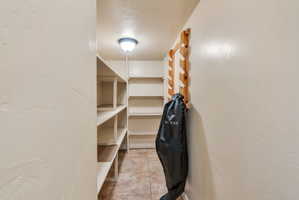 Recessed pantry space featuring extensive built-in shelving, tiled flooring, a flush-mount ceiling light fixture, and a wall-mounted wooden rack