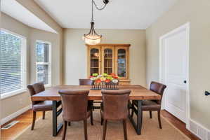 Dining area featuring a bay window, wood-finish flooring, a built-in display cabinet, and a decorative ceiling light fixture
