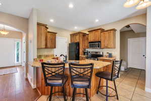 Kitchen with wood cabinetry, granite-style countertops, and a black appliance suite including a refrigerator, range, and microwave
