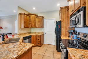Kitchen featuring granite countertops, wood cabinetry, stainless steel appliances, and tile flooring
