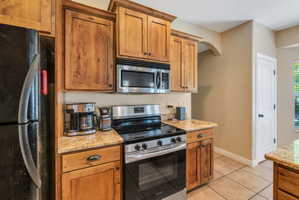 Kitchen featuring wood cabinetry, stainless steel oven/range, built-in microwave, granite-look countertops, and tiled flooring