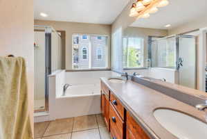 Bathroom featuring a dual vanity with integrated sinks, a built-in jetted tub, a glass-enclosed shower, and tiled flooring