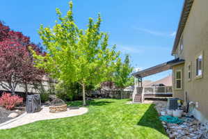 Spacious backyard featuring a covered deck, stone fire pit, and mature trees