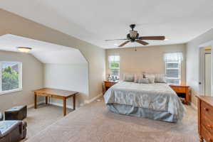 Expansive carpeted room featuring a ceiling fan, dual windows with blinds, a built-in recessed area, and a semi-vaulted ceiling
