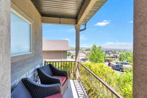 Covered balcony featuring a textured stucco exterior, stone base, and wrought iron railing