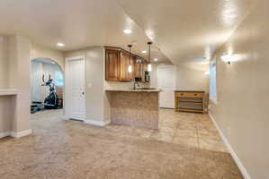 Lower level featuring a tiled wet bar with pendant lighting, wood-finish cabinetry, and a textured tile facade