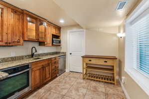 Kitchenette featuring wood cabinetry, granite countertops, tile flooring, and stainless steel appliances