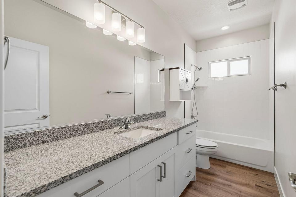 Bathroom featuring a light-toned granite countertop, a single undermount sink with a chrome faucet, and white shaker-style cabinetry with dark hardware