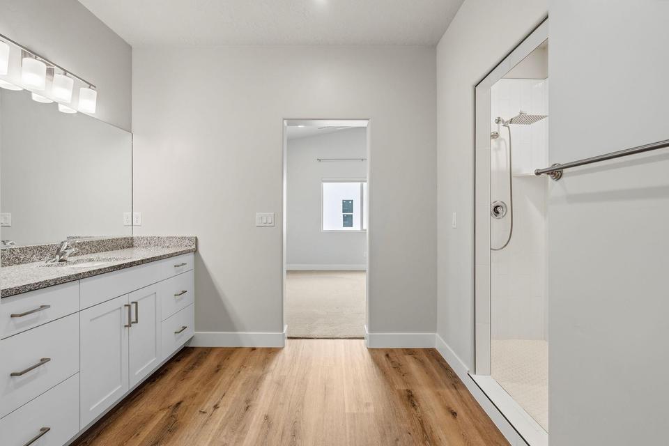 Modern bathroom featuring a double vanity with stone-finish countertop, white cabinetry, and wood-finish flooring
