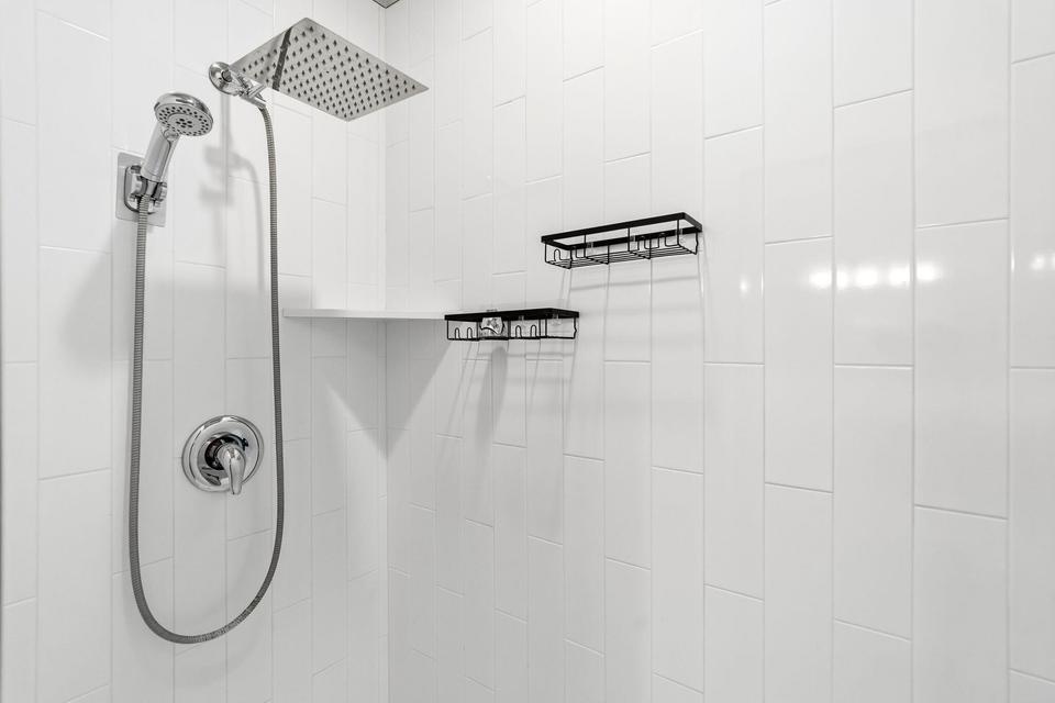 Shower enclosure featuring white subway tile, a rain showerhead, and a handheld shower sprayer