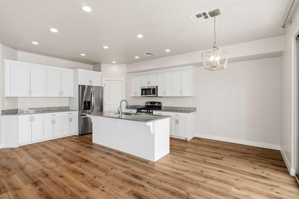 Spacious kitchen featuring an expansive island with an integrated sink, wood-finish flooring, white cabinetry, recessed lighting, and granite countertops