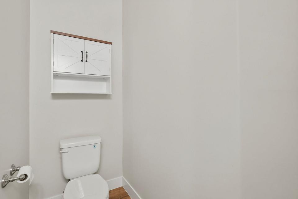 White wall-mounted cabinet with wood-finish top and black hardware, situated above a white toilet