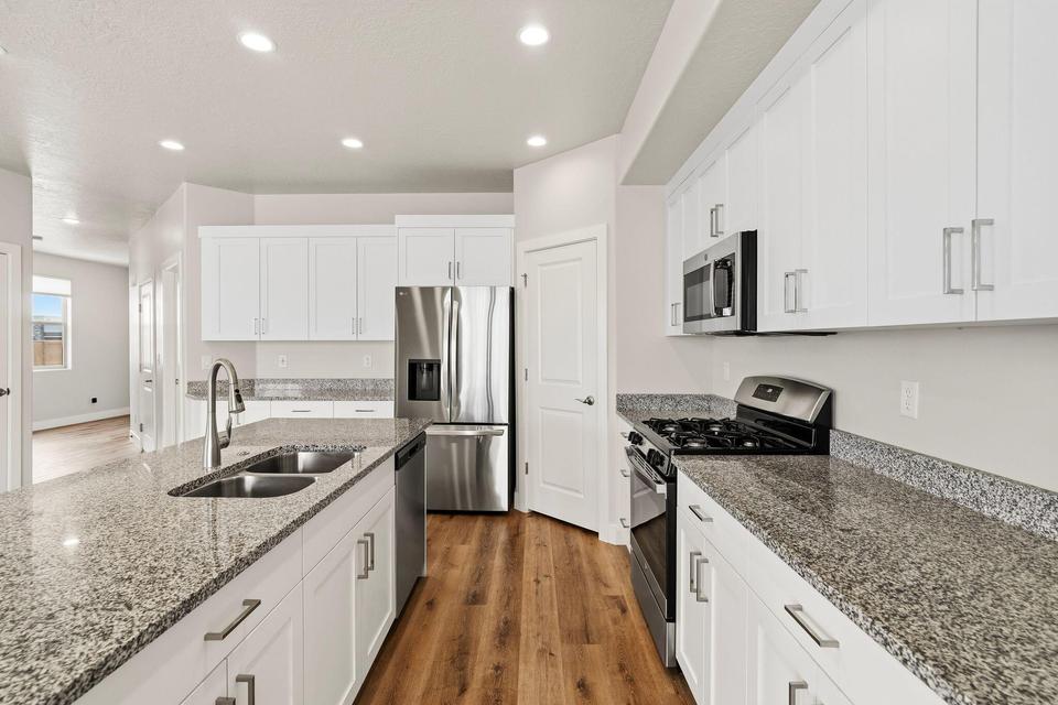 Kitchen featuring white shaker cabinetry, stainless steel appliances, granite countertops, an undermount double basin sink, and wood-finish flooring