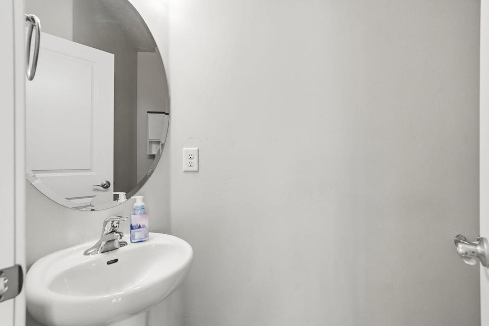 Pedestal sink with a chrome faucet, round wall mirror, and neutral wall paint