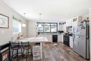 Expansive kitchen featuring wood-finish flooring, white cabinetry, light-colored countertops, and a full suite of black and stainless steel appliances