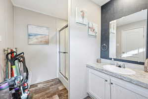 Bathroom featuring a single vanity with a white countertop and oval sink, a wall-mounted mirror, and wood-finish flooring