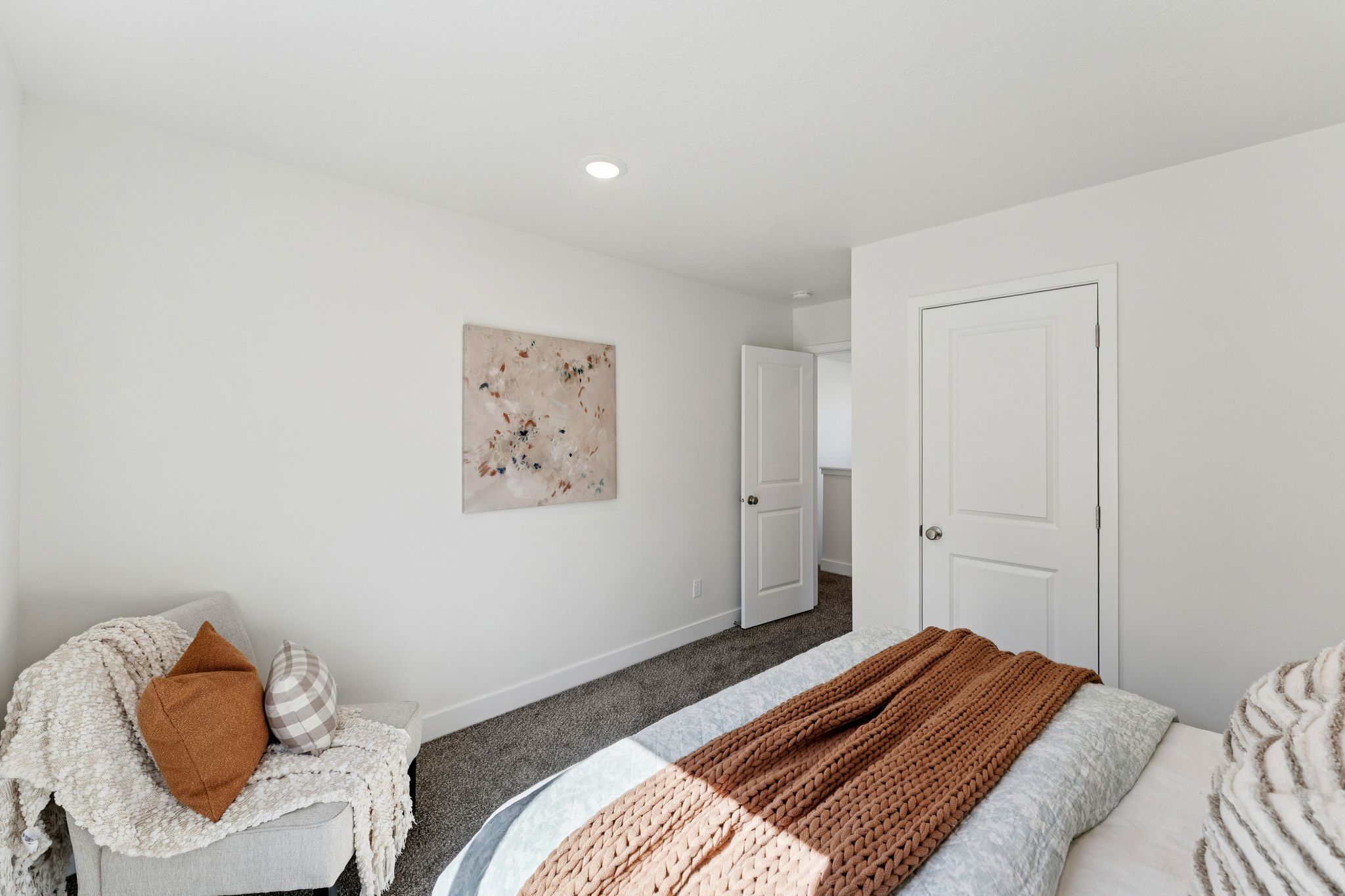 Recessed lighting illuminates a room featuring light-colored walls and dark gray carpeting