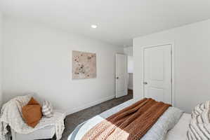 Recessed lighting illuminates a room featuring light-colored walls and dark gray carpeting