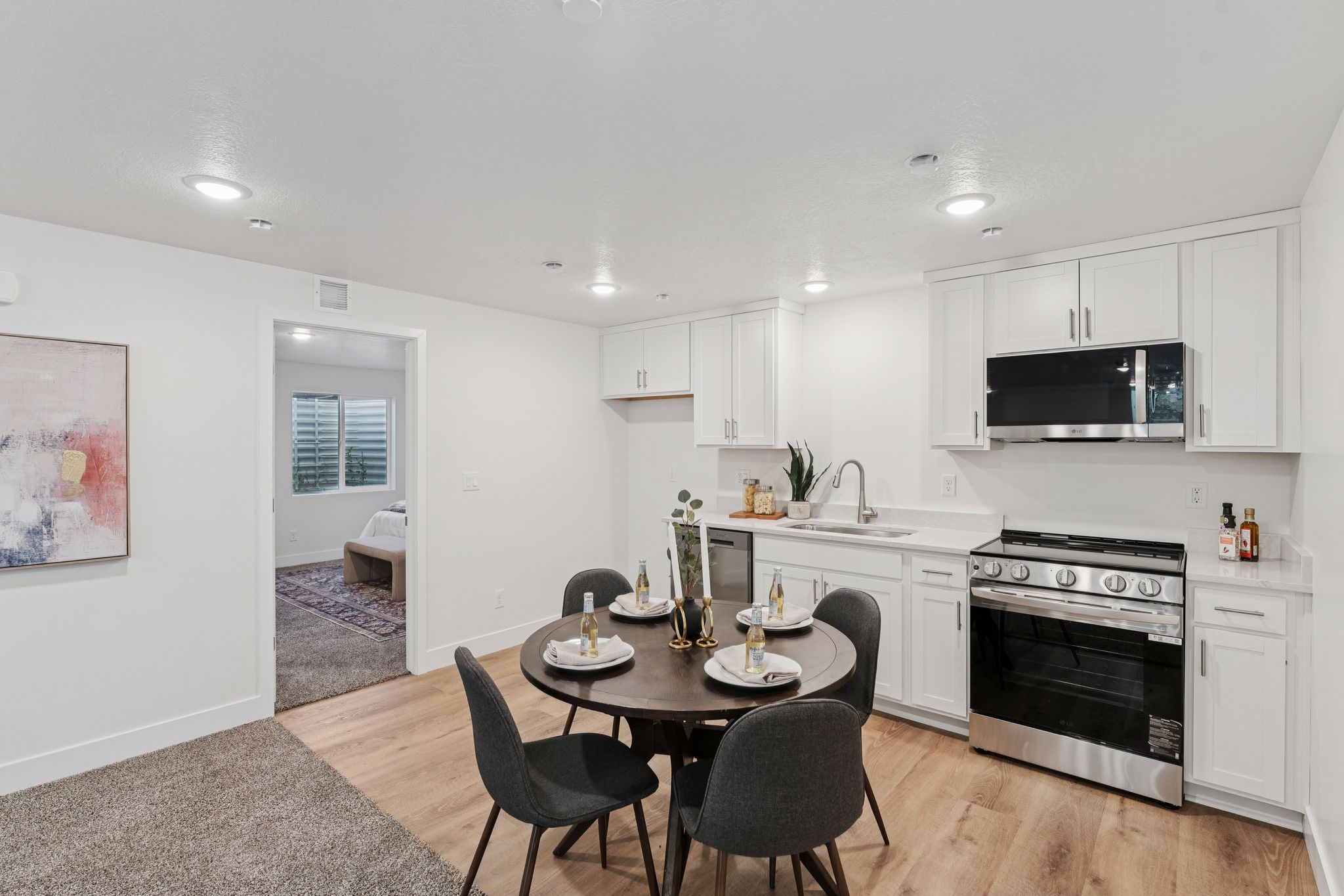 Modern kitchen and dining area featuring wood-finish flooring, white cabinetry, stainless steel appliances, and recessed lighting