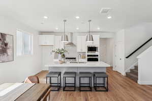 Modern kitchen featuring white cabinetry, a large center island with seating, stainless steel appliances, and wood-finish flooring
