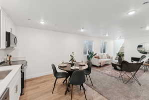 Integrated living space featuring white kitchen cabinetry, stainless steel appliances, and wood-finish flooring