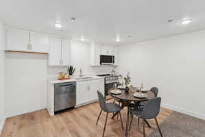 Kitchen area featuring white cabinetry, stainless steel appliances, and wood-finish flooring