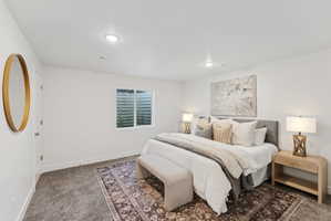 Spacious bedroom featuring neutral wall tones, recessed lighting, a large area rug, and a window with a well-grated exterior