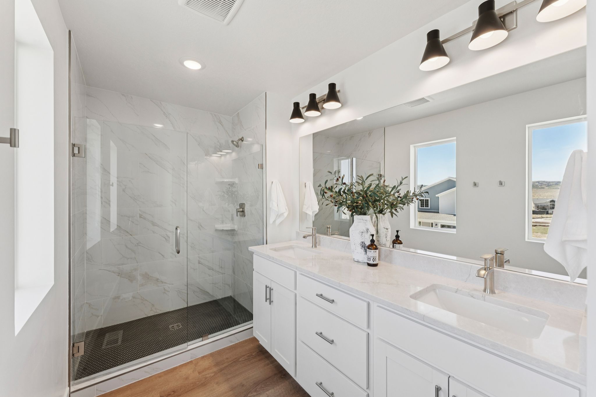 Spacious bathroom featuring a frameless glass shower enclosure with white marbled tile surround and a dark tiled shower pan