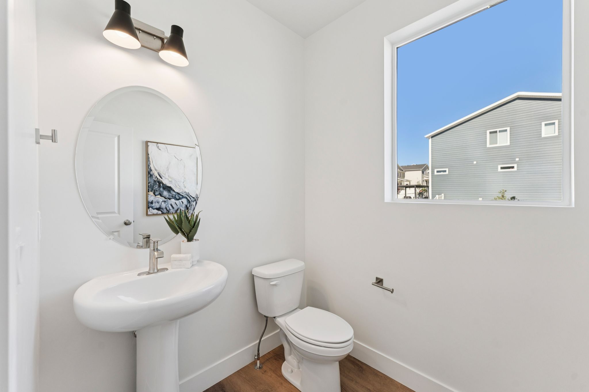 Pedestal sink with a brushed nickel faucet, an oval mirror, and a two-bulb wall sconce