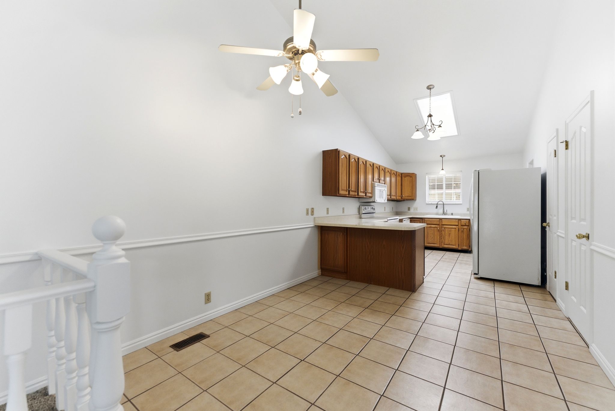 Kitchen area featuring a vaulted ceiling with skylight, tile flooring, and wood-finish cabinetry