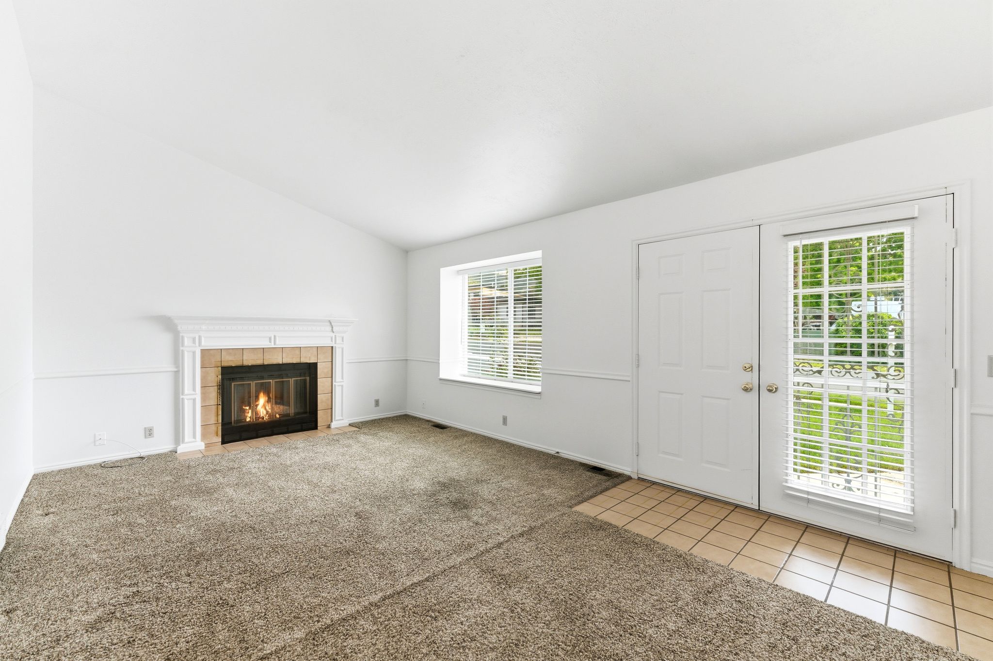 Living area featuring a fireplace with a white mantel and tile surround, a window with blinds, and a door with an accompanying sidelight