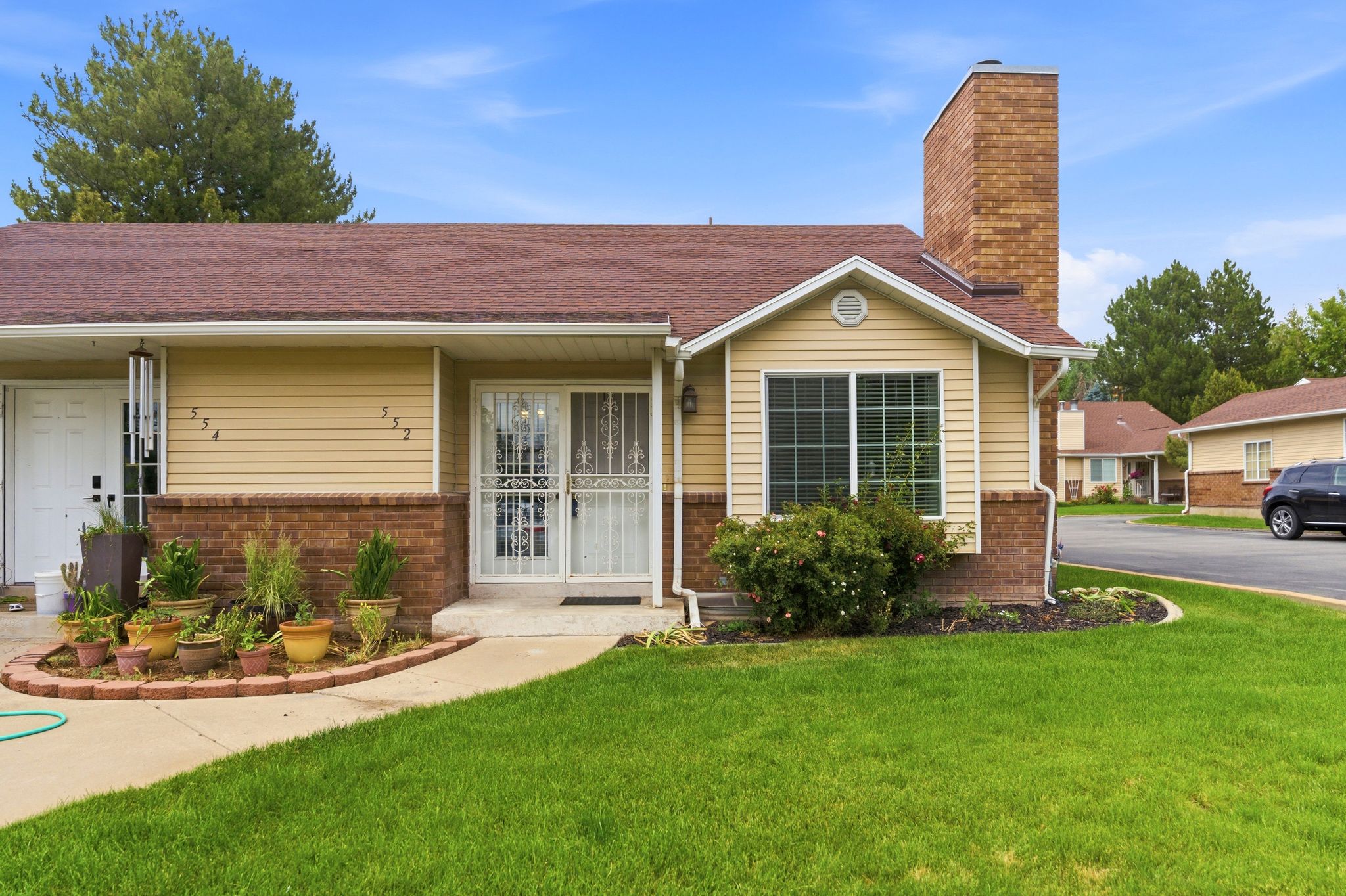 Exterior featuring tan siding, brick facade, a brown shingle roof, and a prominent brick chimney