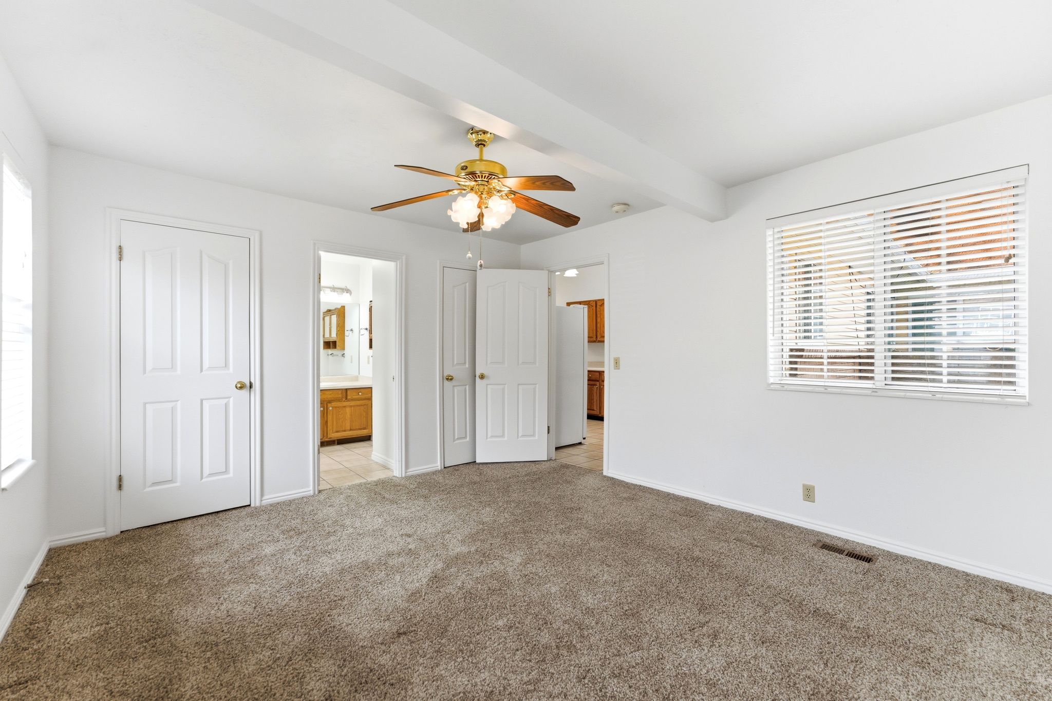 Spacious room featuring neutral carpet flooring, white walls, and a ceiling fan with integrated lighting