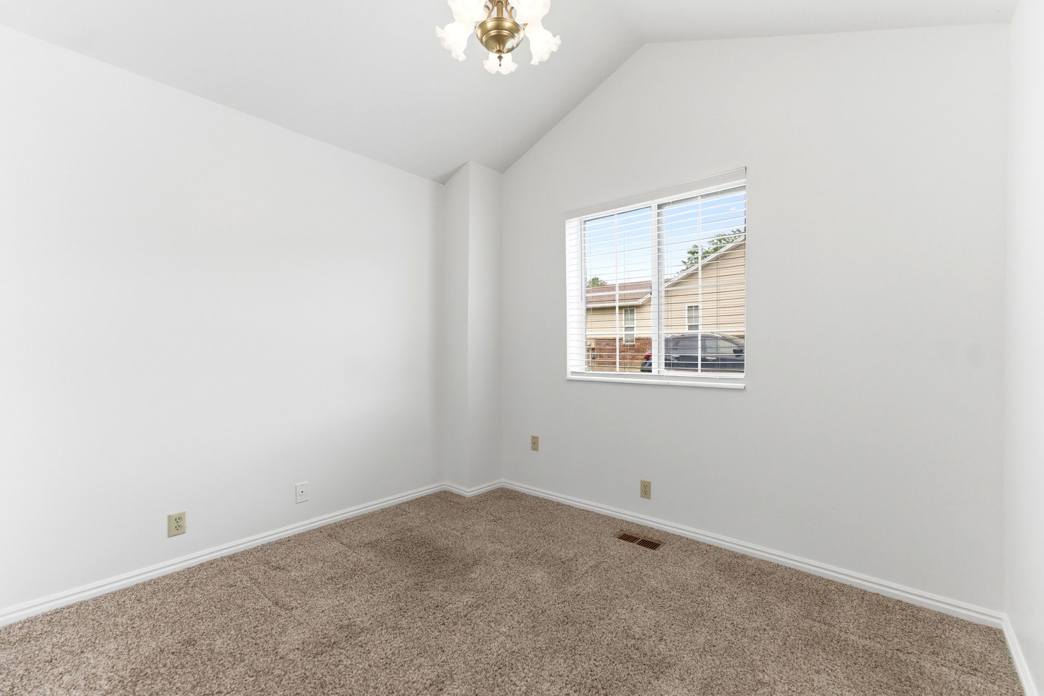 Vaulted ceiling room featuring light brown carpet, white baseboards, and a window with blinds