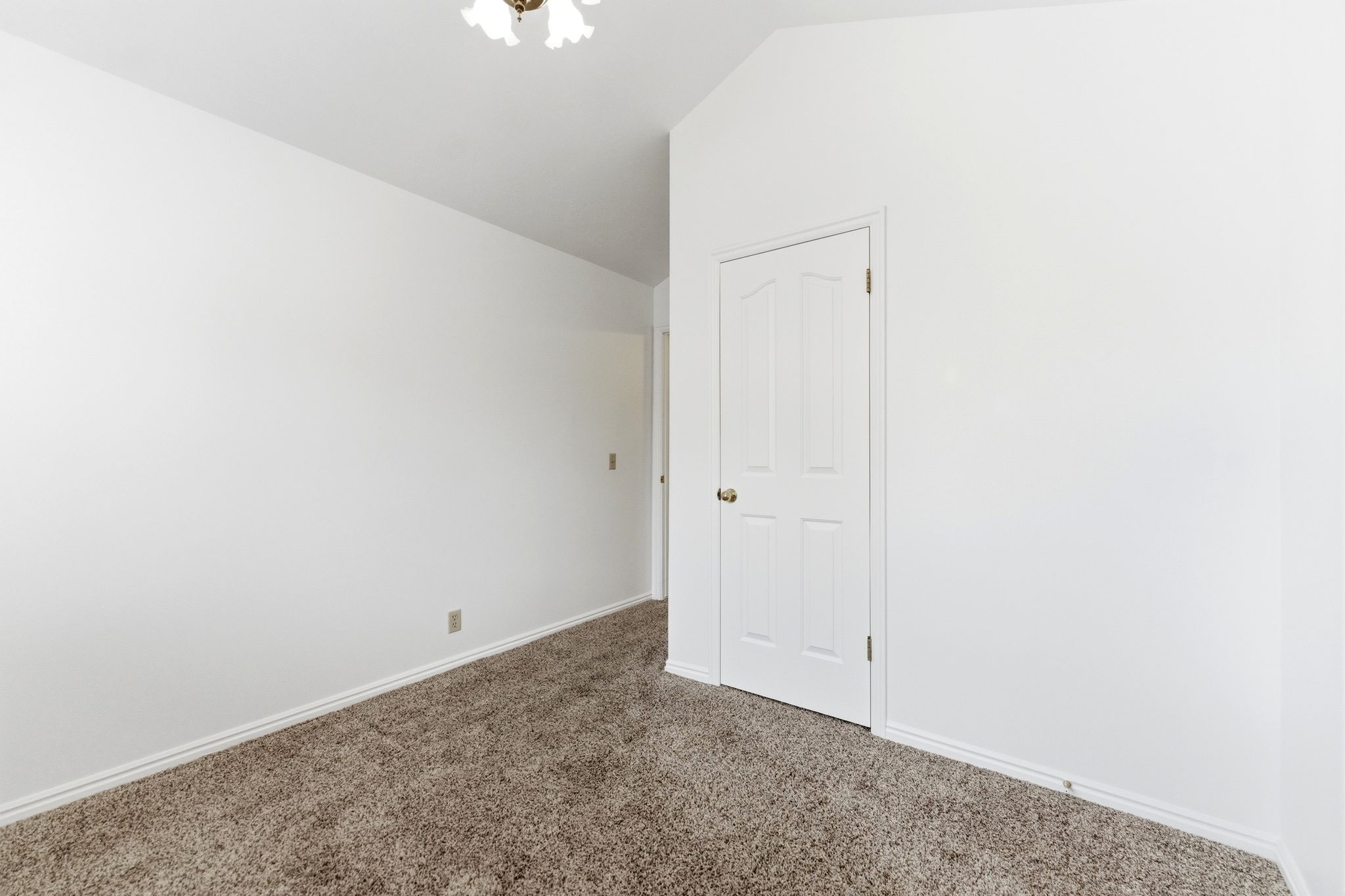 Carpeted room featuring white walls, white trim, a vaulted ceiling, and a white paneled door with a brass-finish doorknob