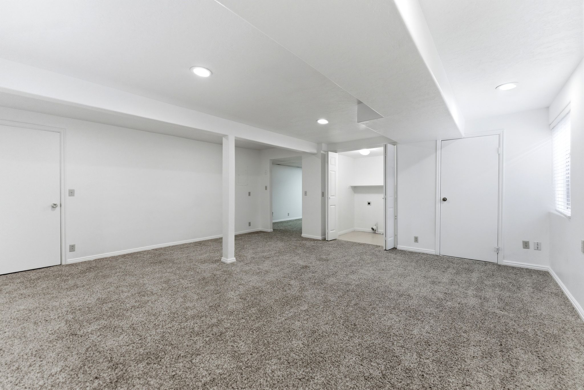 Expansive carpeted area featuring recessed lighting, a utility room with shelving, and a window with blinds