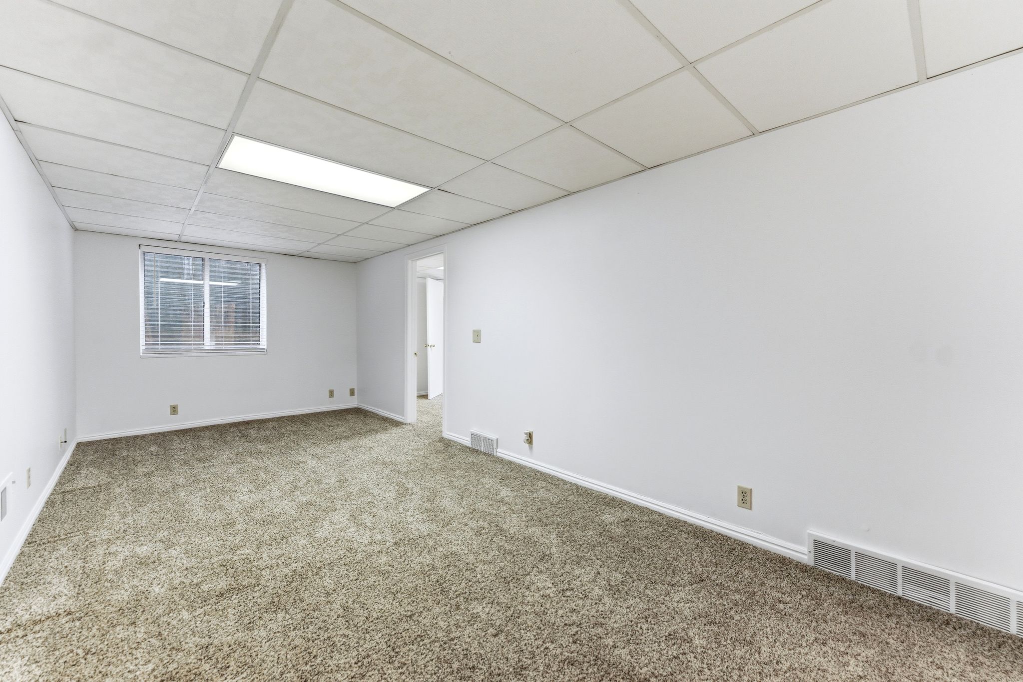 Carpeted room featuring white walls, a grid panel ceiling with recessed lighting, and a window with horizontal blinds