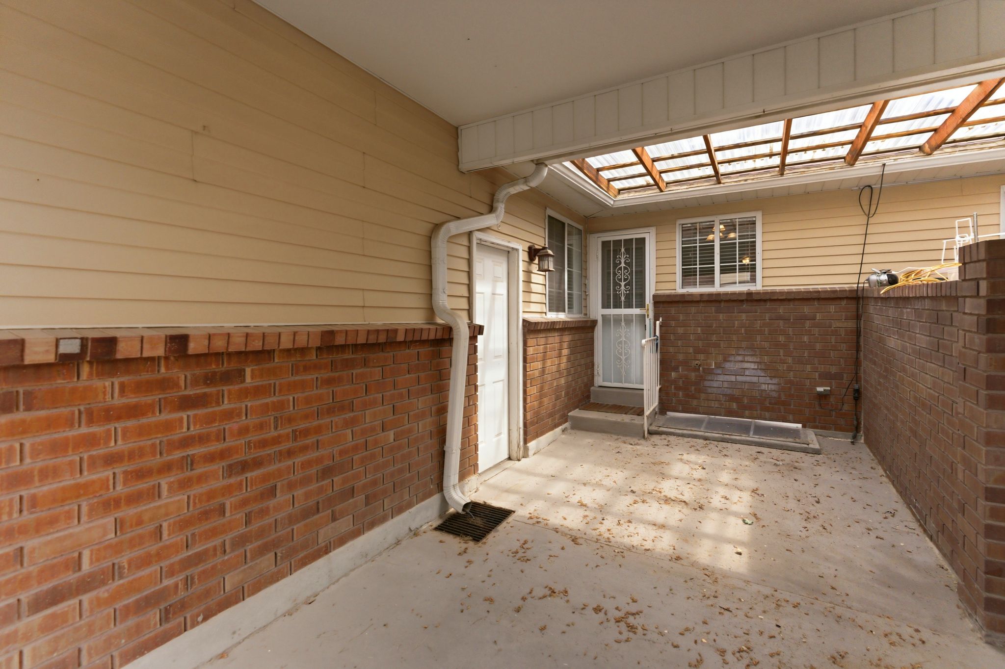 Patio area featuring a translucent slatted roof system, brick half-walls, and tan horizontal siding