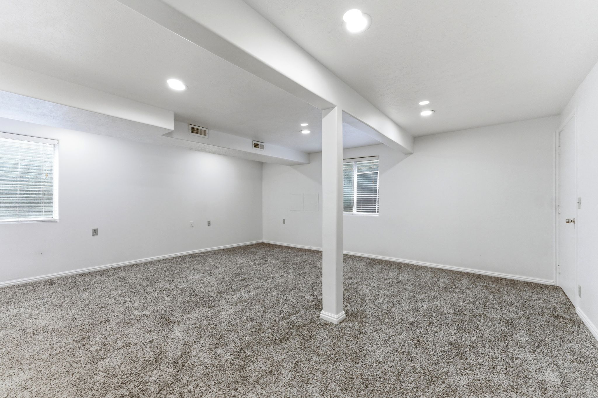 Finished basement space featuring recessed lighting, a neutral carpet, two windows with blinds, and white painted walls